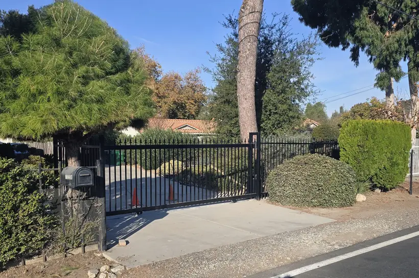 Custom wrought iron sliding gate with finial tops beside block wall