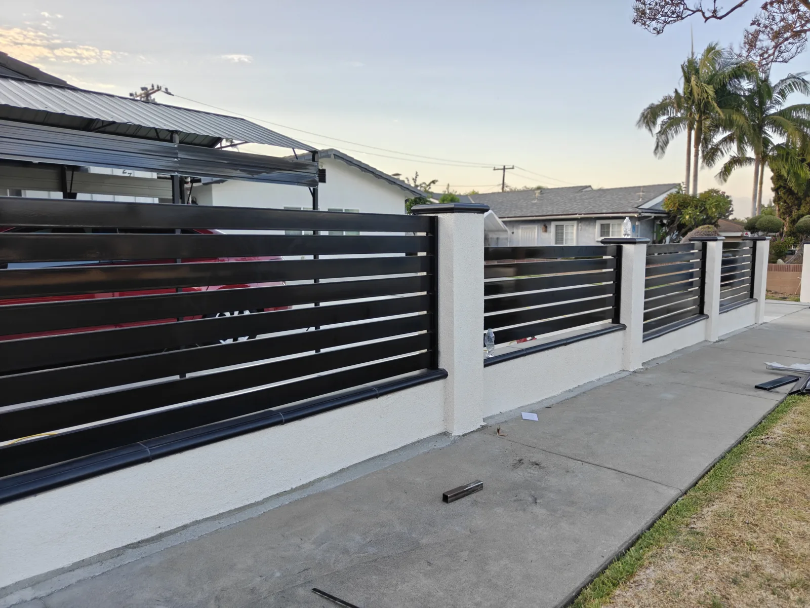 Long run of modern black horizontal slat fencing on a white stucco block wall at dusk in La Puente, CA by Apexguard Fence