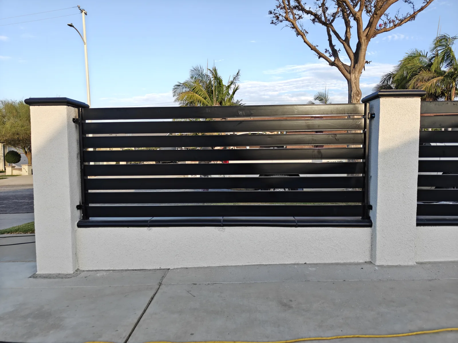 Black powder-coated horizontal slat fence panel between white stucco CMU pilasters in La Puente, CA by Apexguard Fence