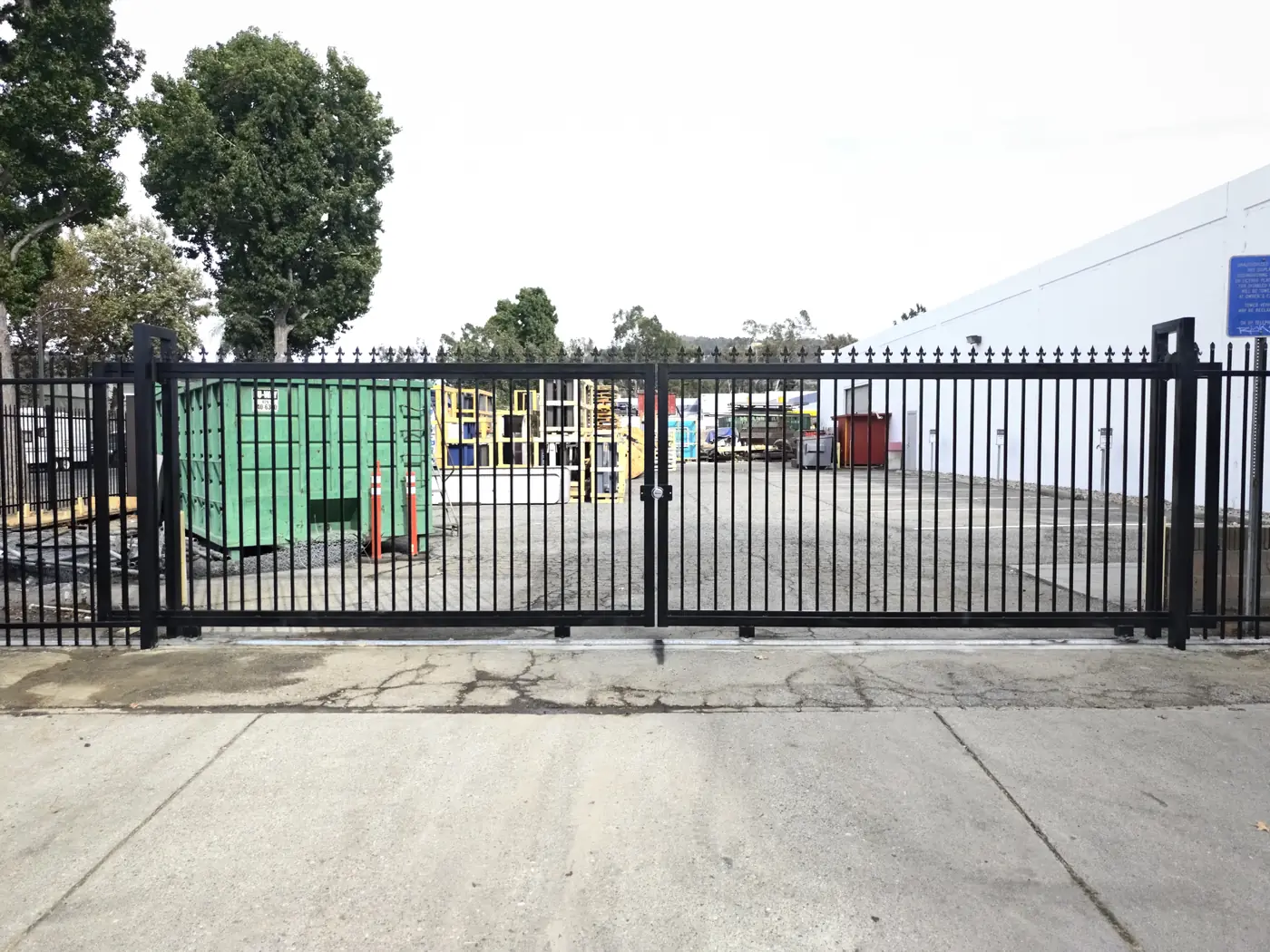 Completed 24 ft bi-parting sliding gate closed across a commercial yard driveway in Whittier, CA, two 12 ft leaves meeting at a center stop