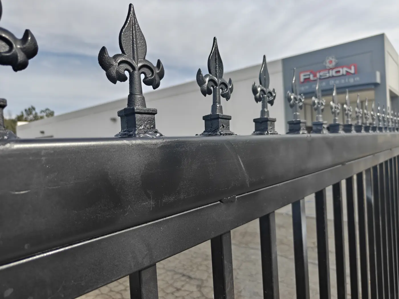 Close-up of cast fleur-de-lis finials on the top rail of a 7 ft commercial steel gate at the Fusion Sign & Design facility in Whittier, CA