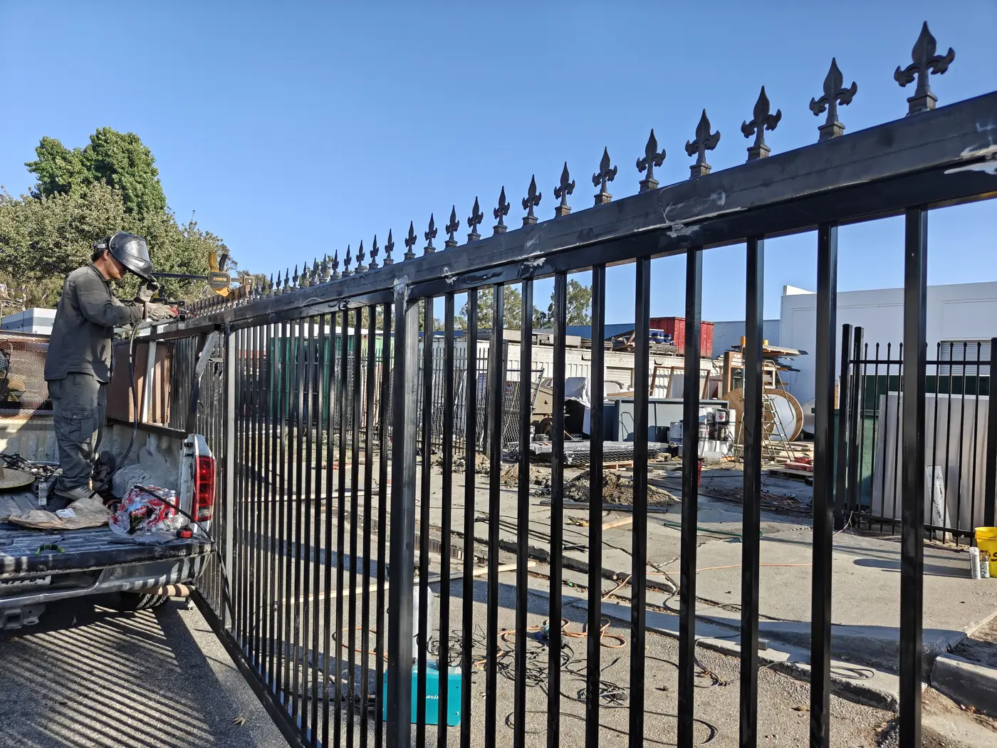 Welding cast fleur-de-lis finials onto the top rail of a commercial steel sliding gate in Whittier, CA